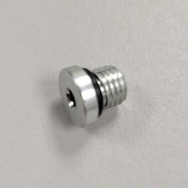 Close-up of a metallic hex-head threaded plug with an internal hexagonal recess, on a plain white background.