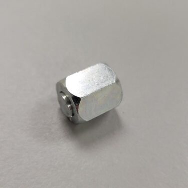 A silver hexagonal nylock nut with a nylon insert visible from the side, placed on a grey surface